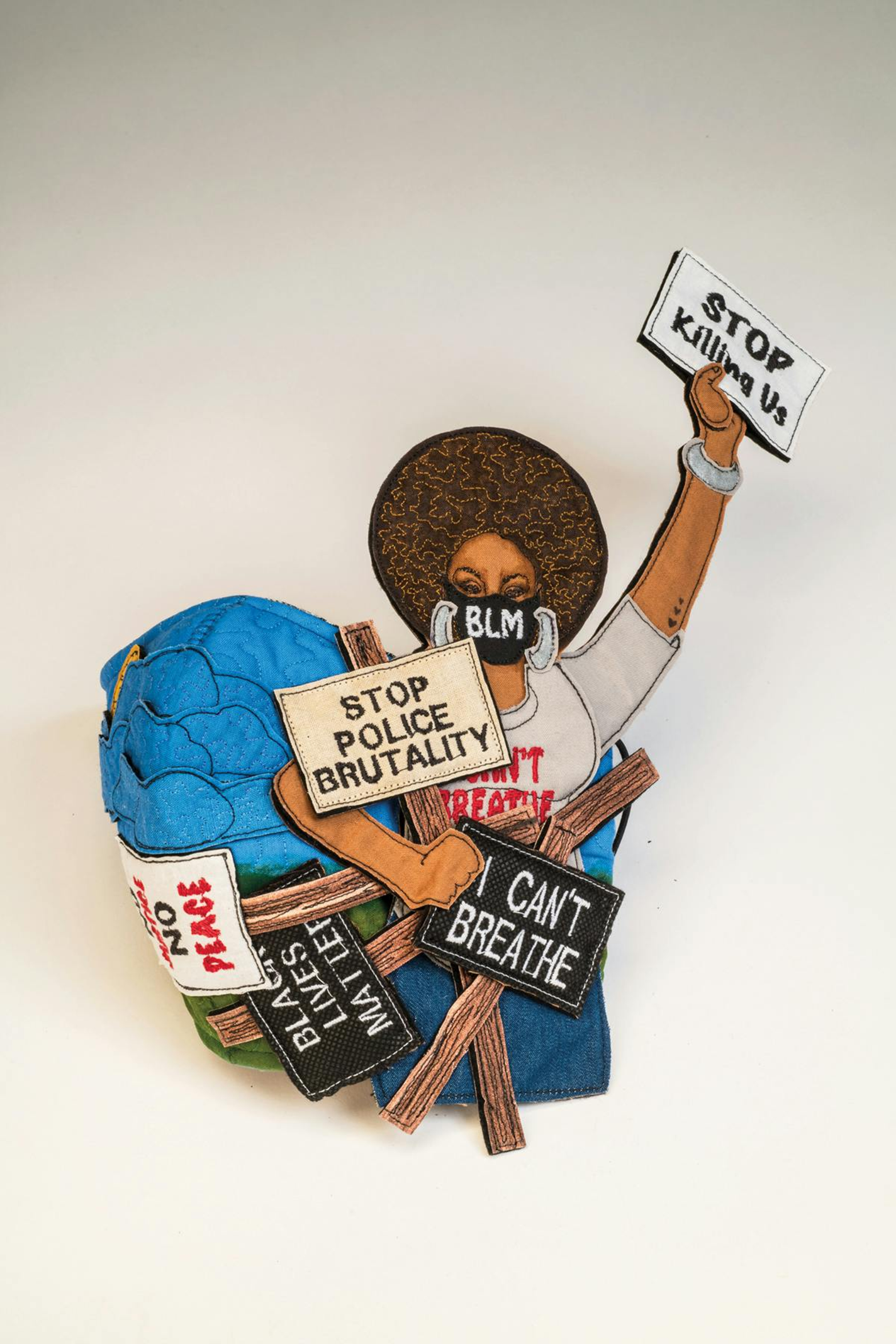 Representational fiber art piece depicting a protestor wearing a BLM face mark and holding a collection of protest signs