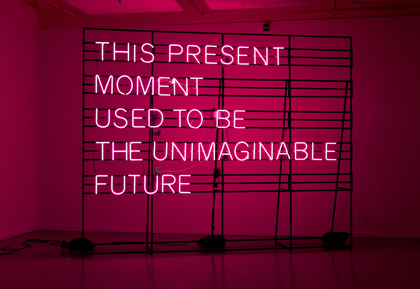 Large installation piece with the phrase THIS PRESENT MOMENT USED TO BE THE UNIMAGINABLE FUTURE in pink neon.