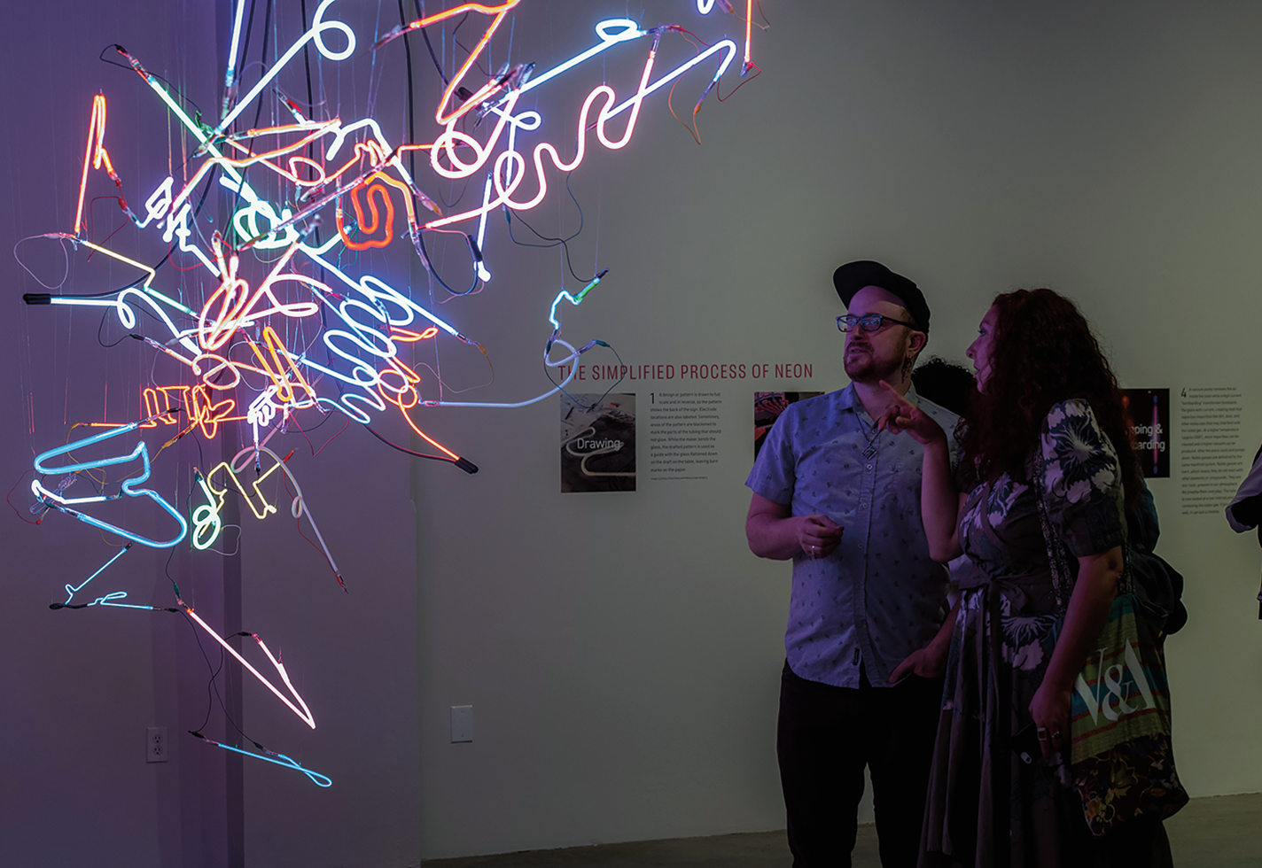 Museum goers looking at neon art piece suspended from ceiling