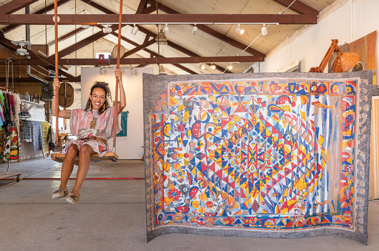 Paula Wilson sits on a swing inside her studio next to a painted rug.