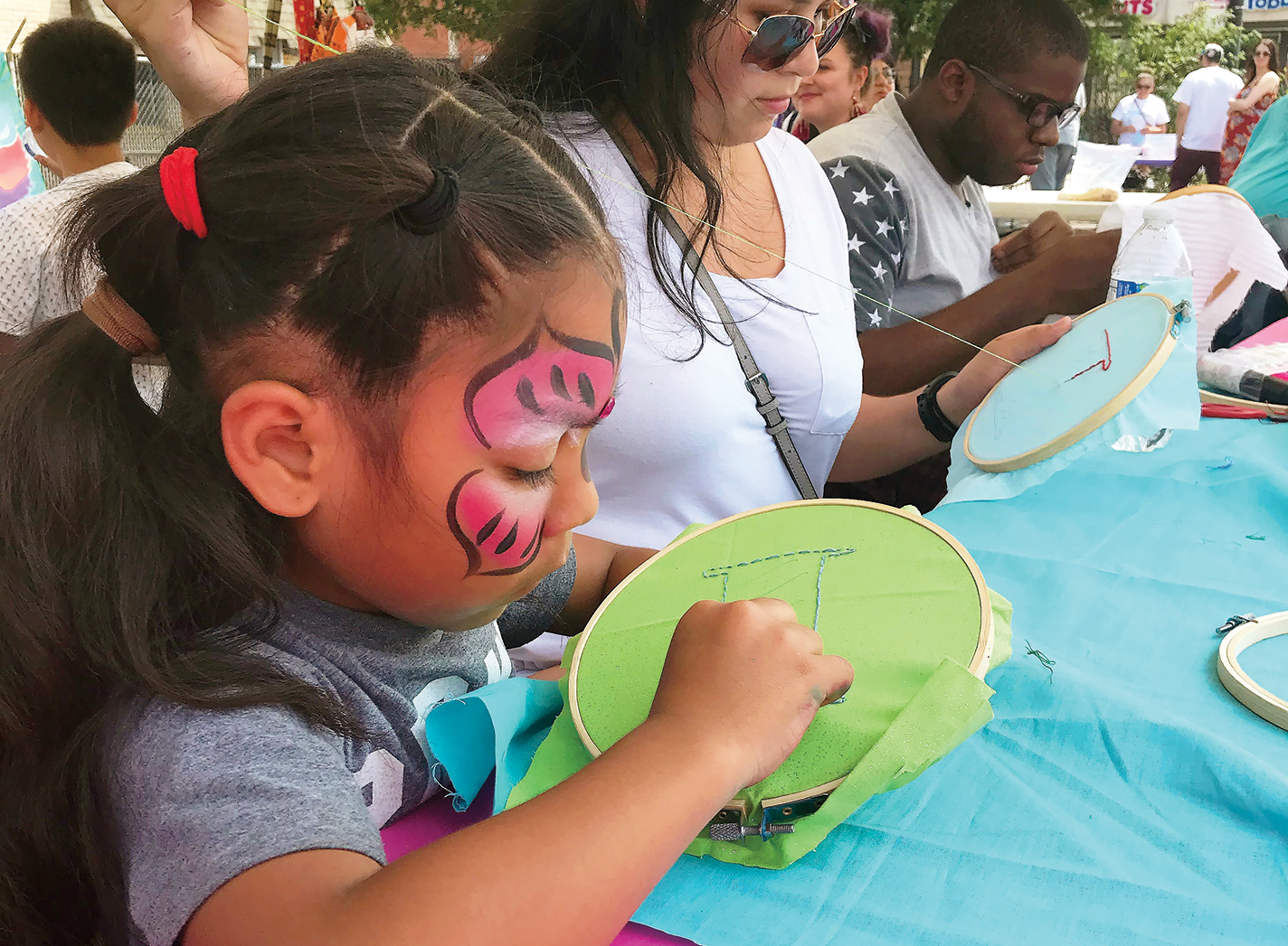 Child with face paint doing a cross-stitch project