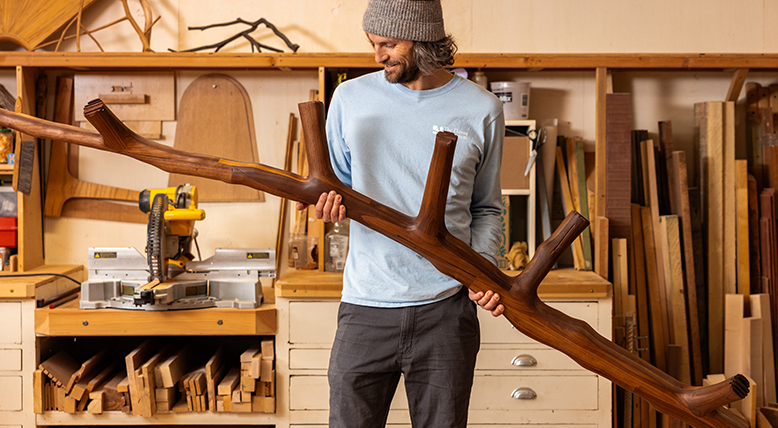 Kevin Reiswig holds a tree branch-shaped sculpture crafted from reclaimed wood.