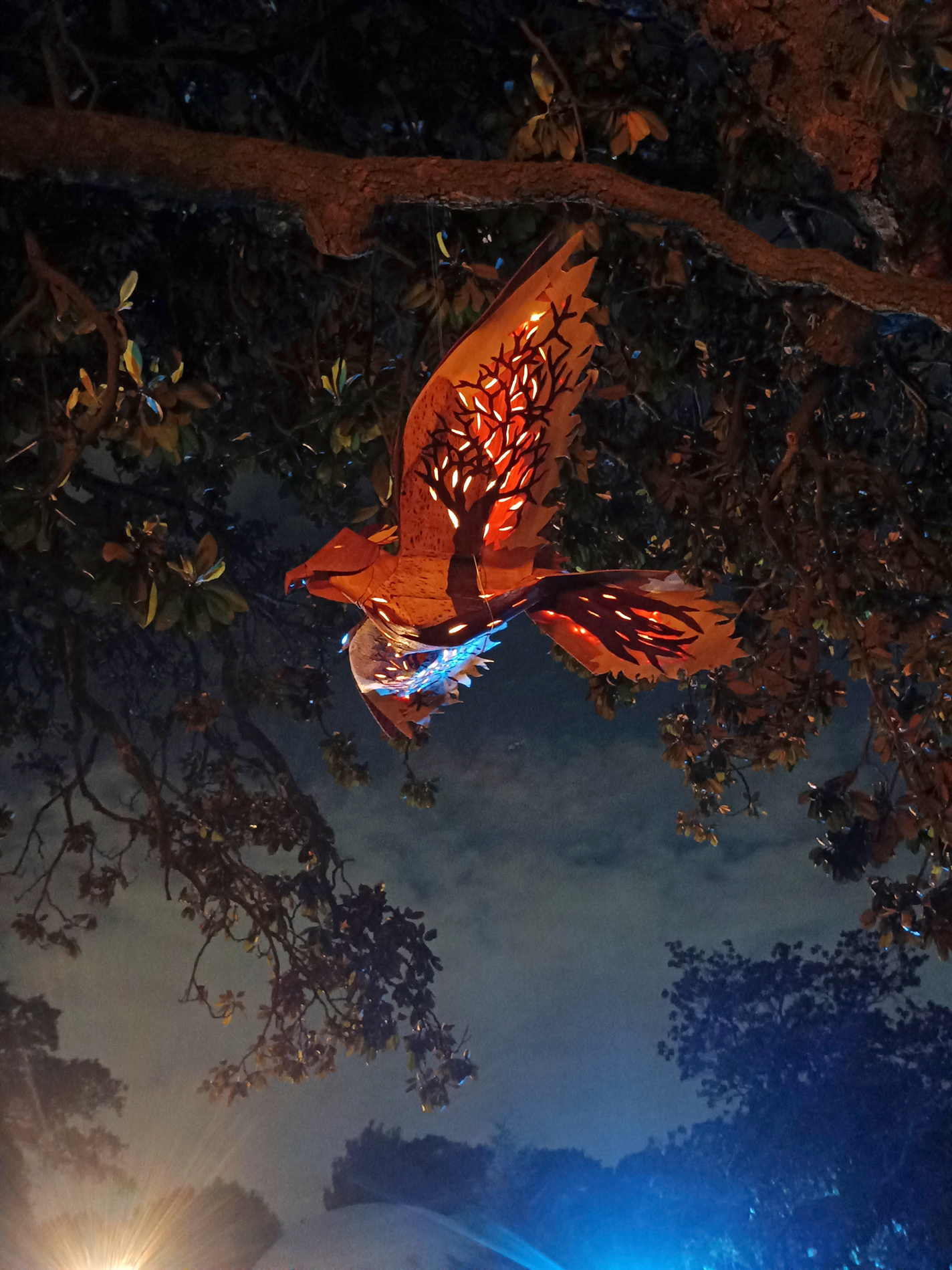 Illuminated wooden bird statue hanging from a tree