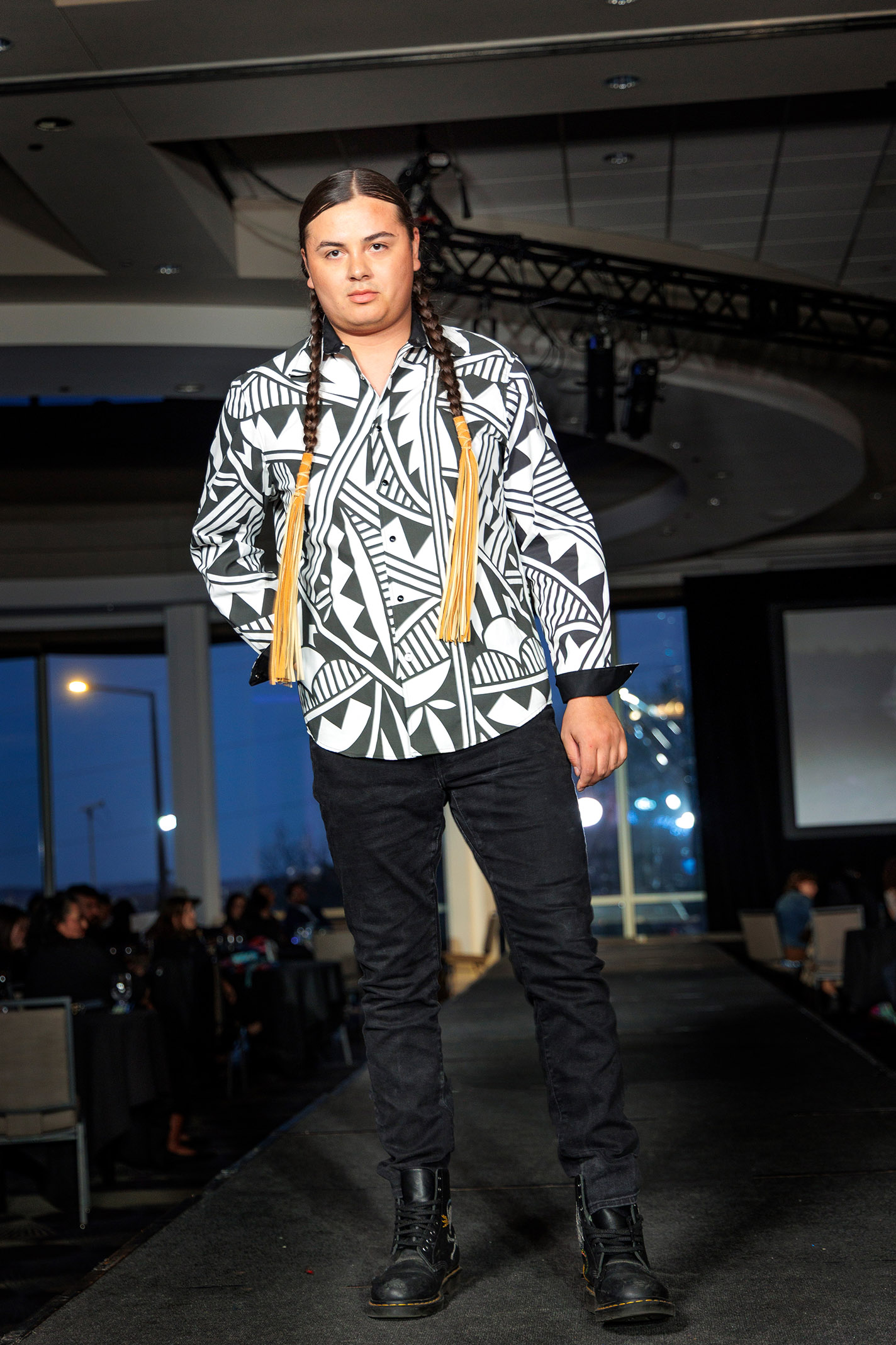 Model wears patterned shirt and long, tasseled braids on the runway.