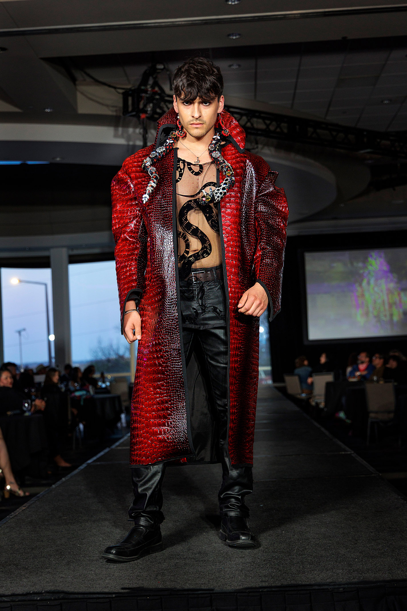 Model wears a long cape and translucent snake-patterned top on the runway.
