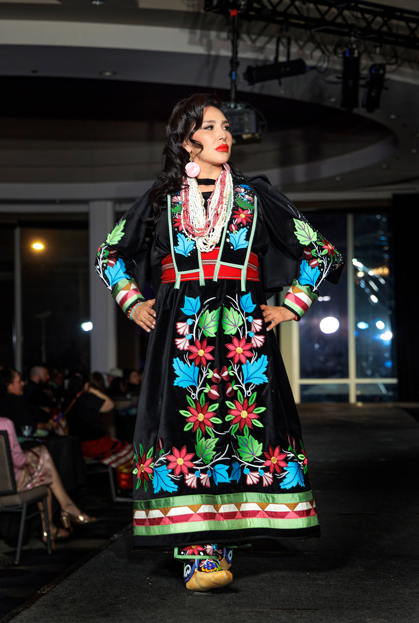 Model wears a long dress with a traditional floral motif on the runway.